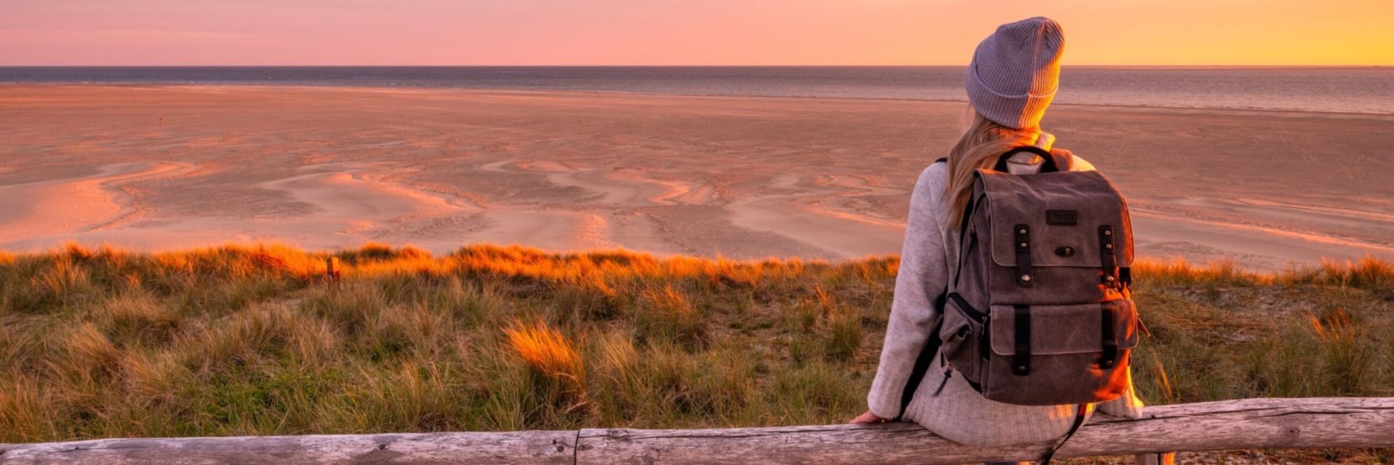 Wandelaar met rugzak kijkt bij zonsondergang vanaf de duinen over het strand van Texel